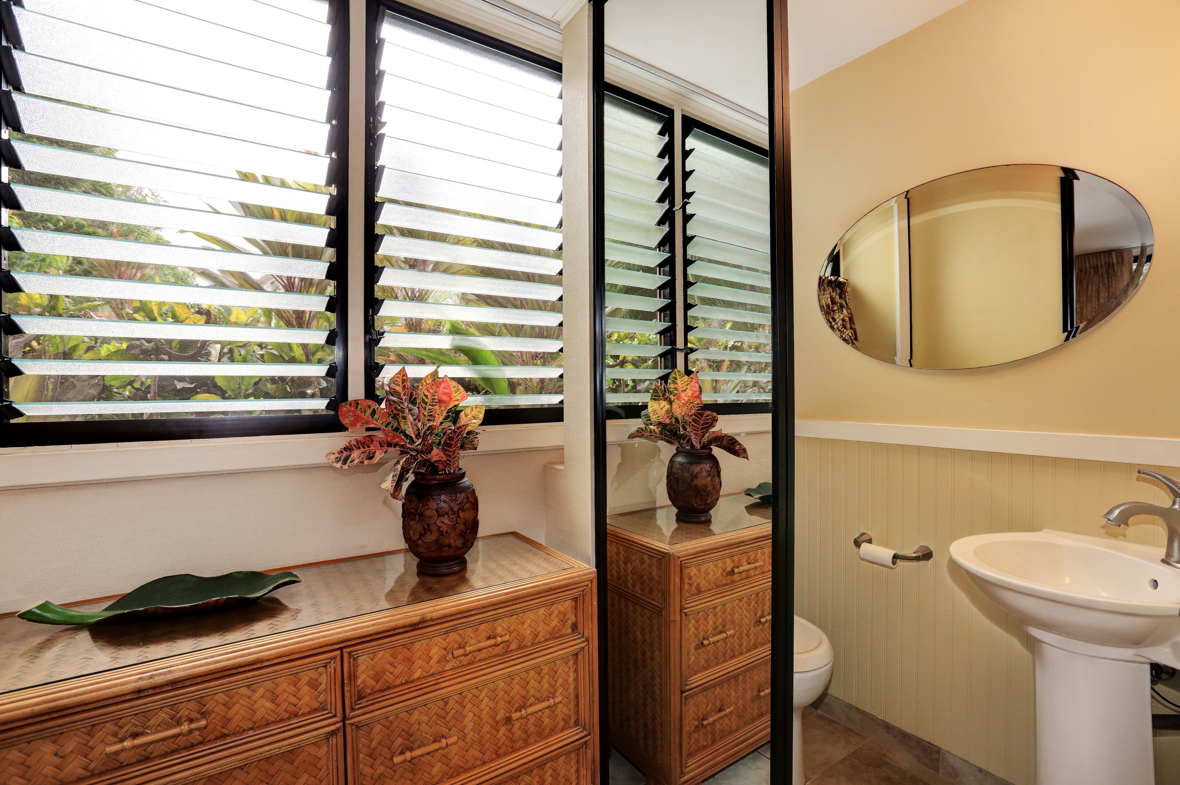 A bathroom with a wooden vanity, a sink, a mirror, and a window with blinds.