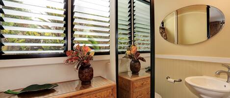 A bathroom with a wooden vanity, a sink, a mirror, and a window with blinds.