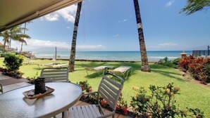 A patio with a table and chairs overlooking a beach with palm trees and a clear sky. - Pikake #a6 2 Bedroom Condo by RedAwning (Lahaina)