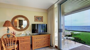 A room with a television, wicker furniture, a mirror, and a view of the ocean. - Pikake #a6 2 Bedroom Condo by RedAwning (Lahaina)