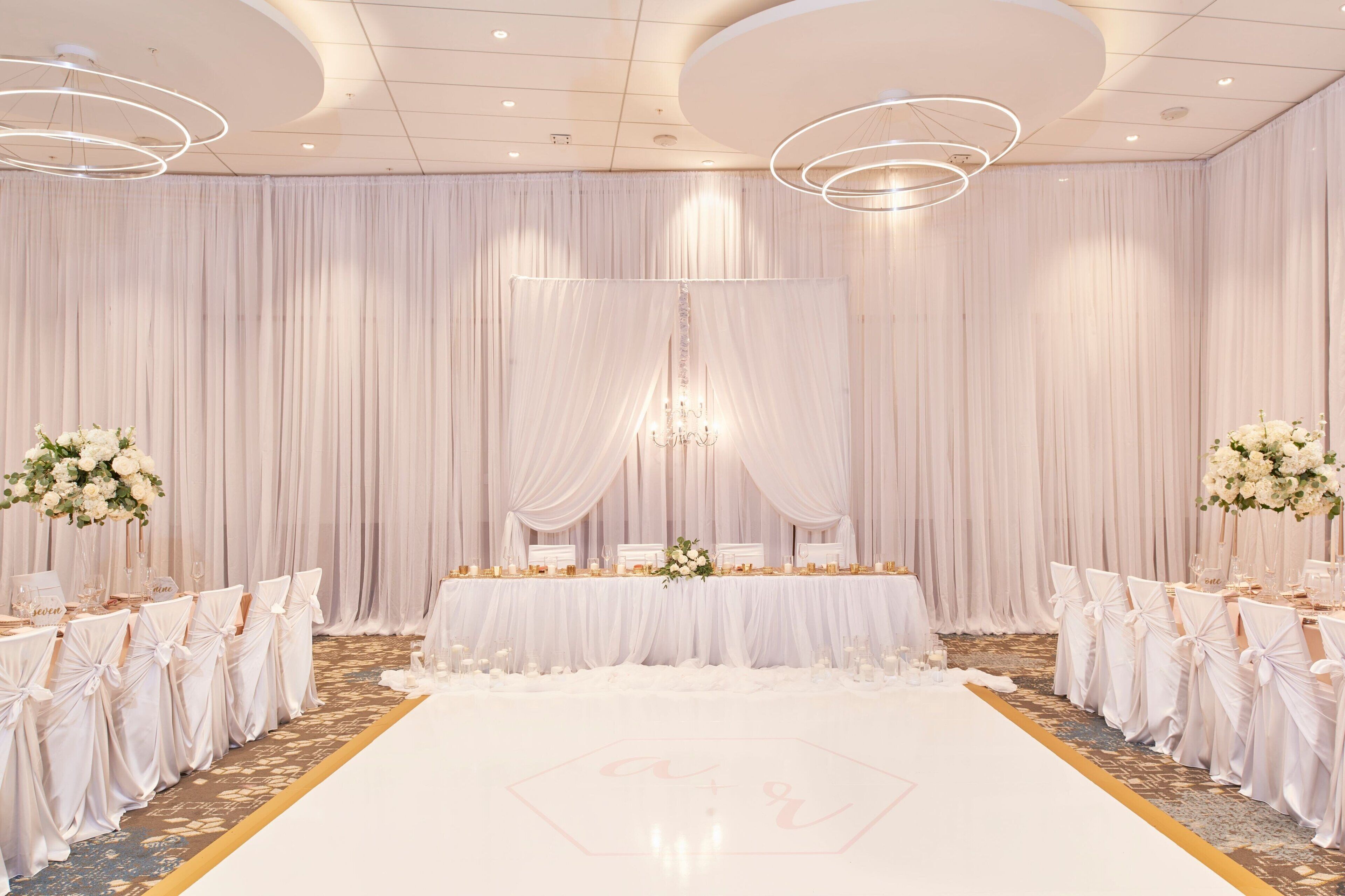 A wedding reception area with a white floor, draped curtains, and a table set for guests.
