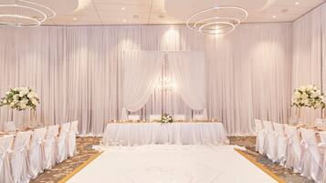 A wedding reception area with a white floor, draped curtains, and a table set for guests.