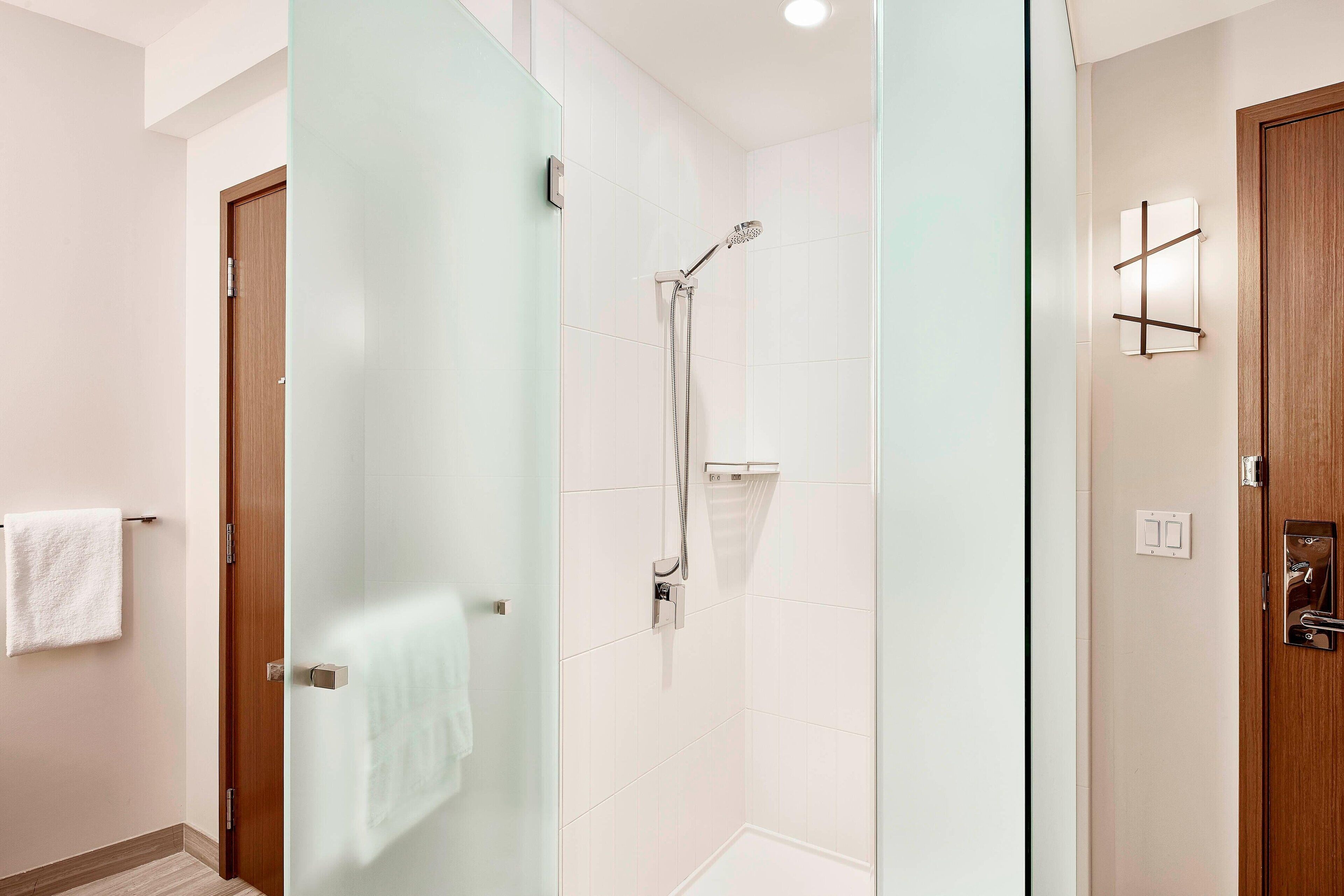 Un baño moderno con cabina de ducha de vidrio, una puerta de madera y una toalla blanca colgada en la pared.