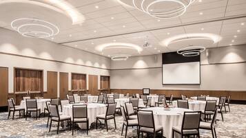 A conference room with round tables, chairs, a projector screen, and a large screen.