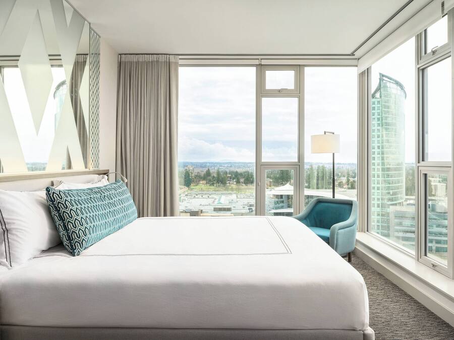 A hotel room with a large bed, a view of the city, and a modern chair.