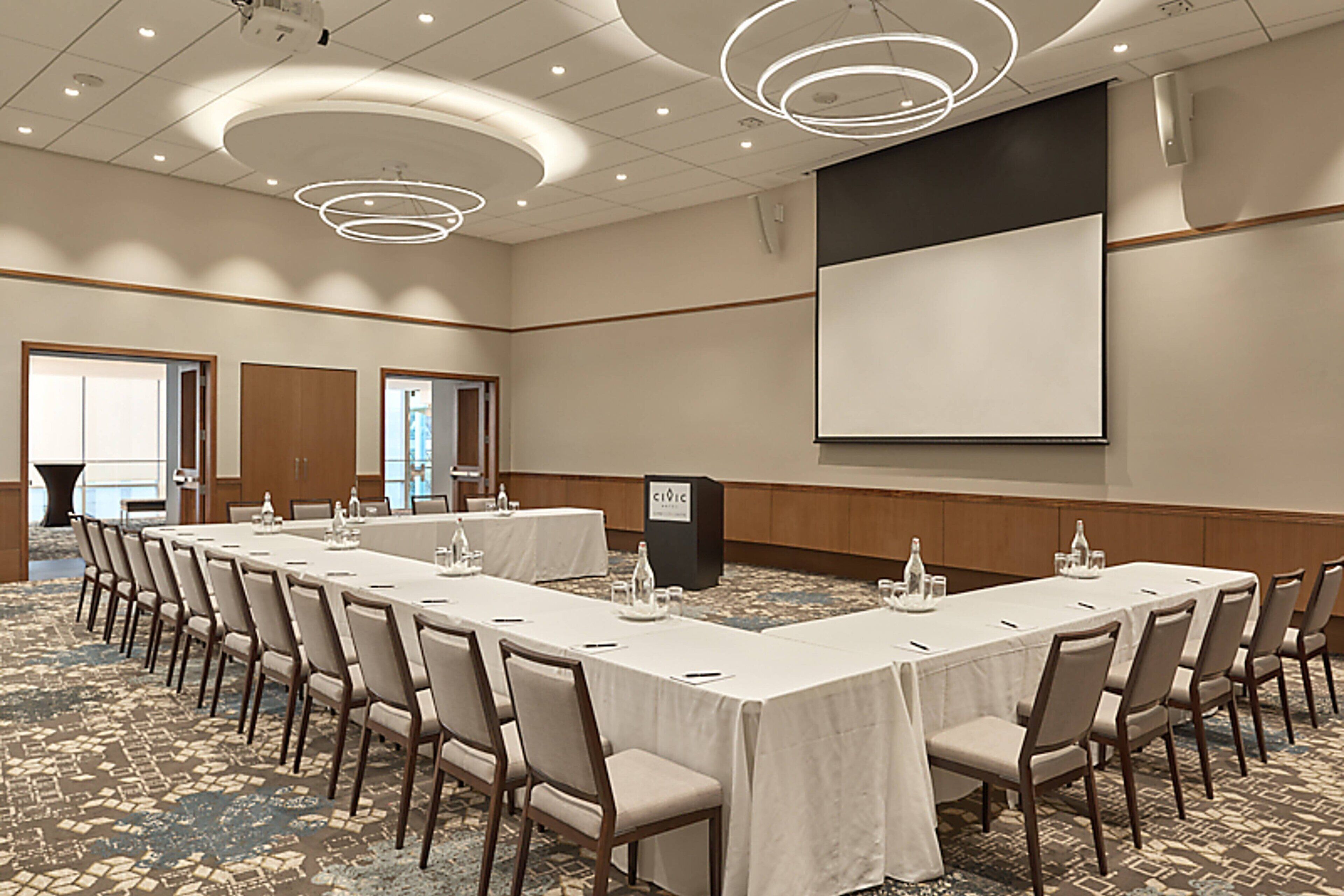 Un salón de conferencias con una larga mesa, sillas, una pantalla de proyector y un atril.