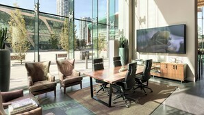 A modern conference room with a large glass window, leather chairs, a wooden table, and a flat-screen TV. - Civic Hotel Autograph Collection (Surrey)