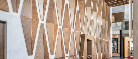 Un interior moderno con paneles de madera geométricos, una escalera de metal y una zona de estar roja.