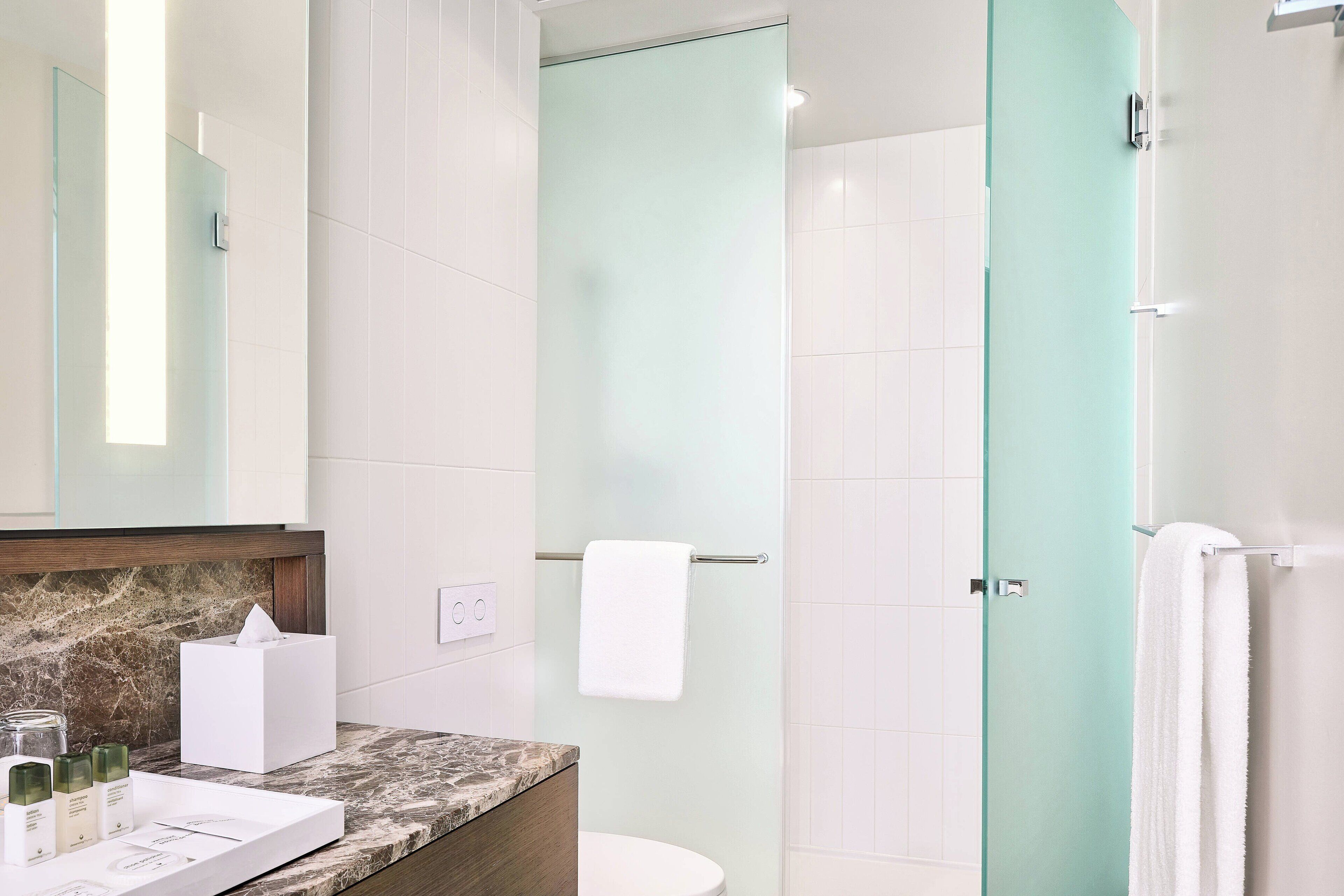 A modern bathroom with a marble countertop, a glass shower enclosure, and a white toilet.