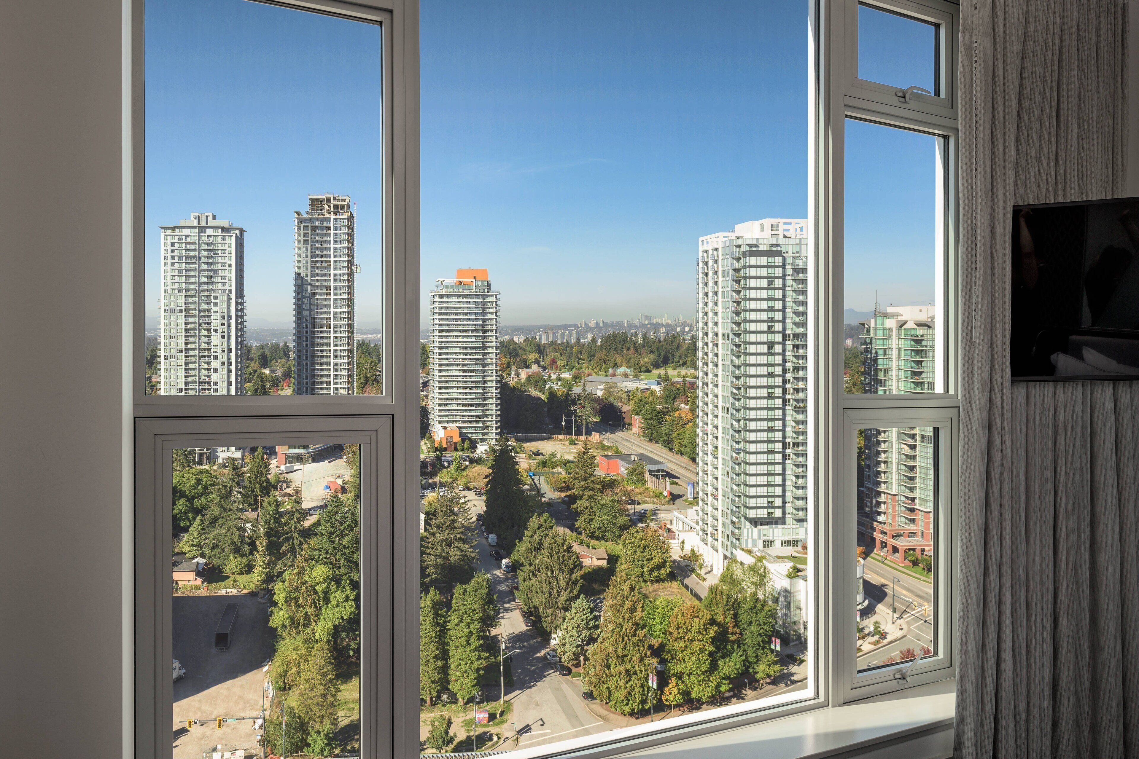 Un edificio alto con numerosas ventanas y balcones, que ofrece vistas de un paisaje urbano con otros edificios y zonas verdes.