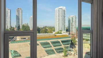 A view through a window of a high-rise building with multiple floors, large windows, and a green roof.