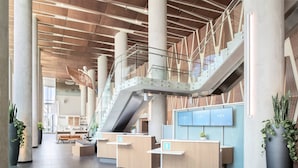 A modern lobby with a central staircase, reception desks, and large potted plants. - Civic Hotel Autograph Collection (Surrey)