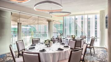 A conference room with round tables, chairs, and a large window with a view of buildings.