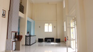 Um hall amplo com balcão de recepção, área de estar e grandes janelas que proporcionam iluminação natural.