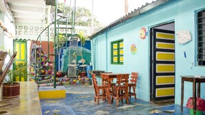 A colorful courtyard with a blue building, a wooden table and chairs, and a fountain. - Hostel Villa Mary (Santa Marta)
