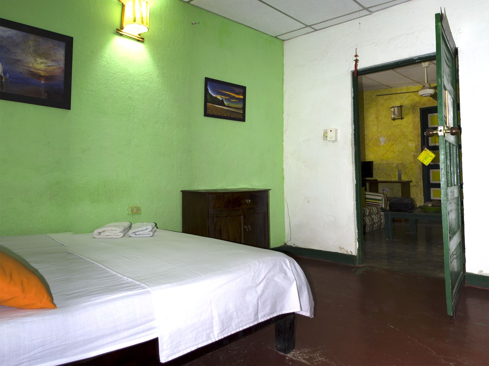 Quarto com cama, pequeno armário, luminária na parede e porta para outro cômodo.