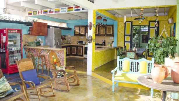 A kitchen with wooden cabinets, a refrigerator, and a microwave. There is a dining area with a table and chairs. - Hostel Villa Mary (Santa Marta)