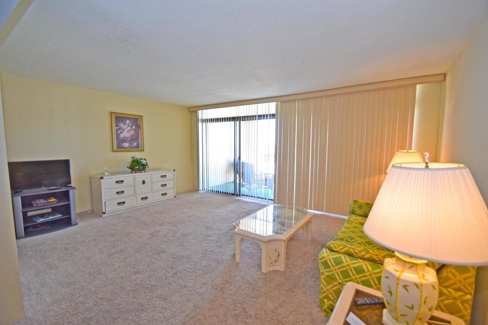 A living room with a sofa, a coffee table, a TV stand, a cabinet, and a sliding glass door leading to a balcony.