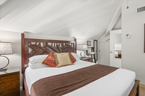 A bedroom with a wooden headboard, a bed with white bedding and a brown throw, a bedside table with a lamp, and a door with a mirror. - Maui Kaanapali S #b233 1 Bedroom Condo by RedAwning (Lahaina)