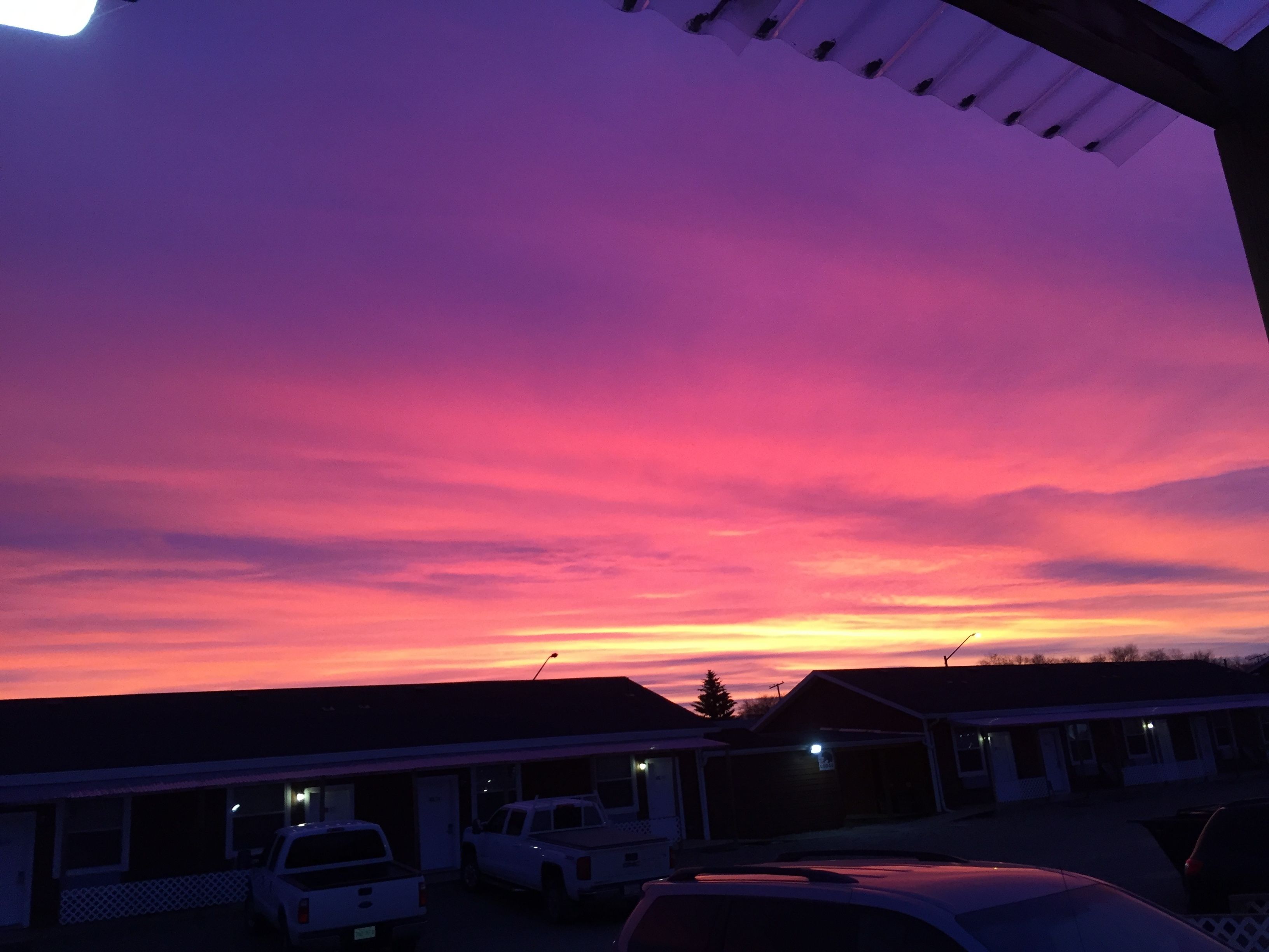 A sunset over a row of buildings with parked cars in front.