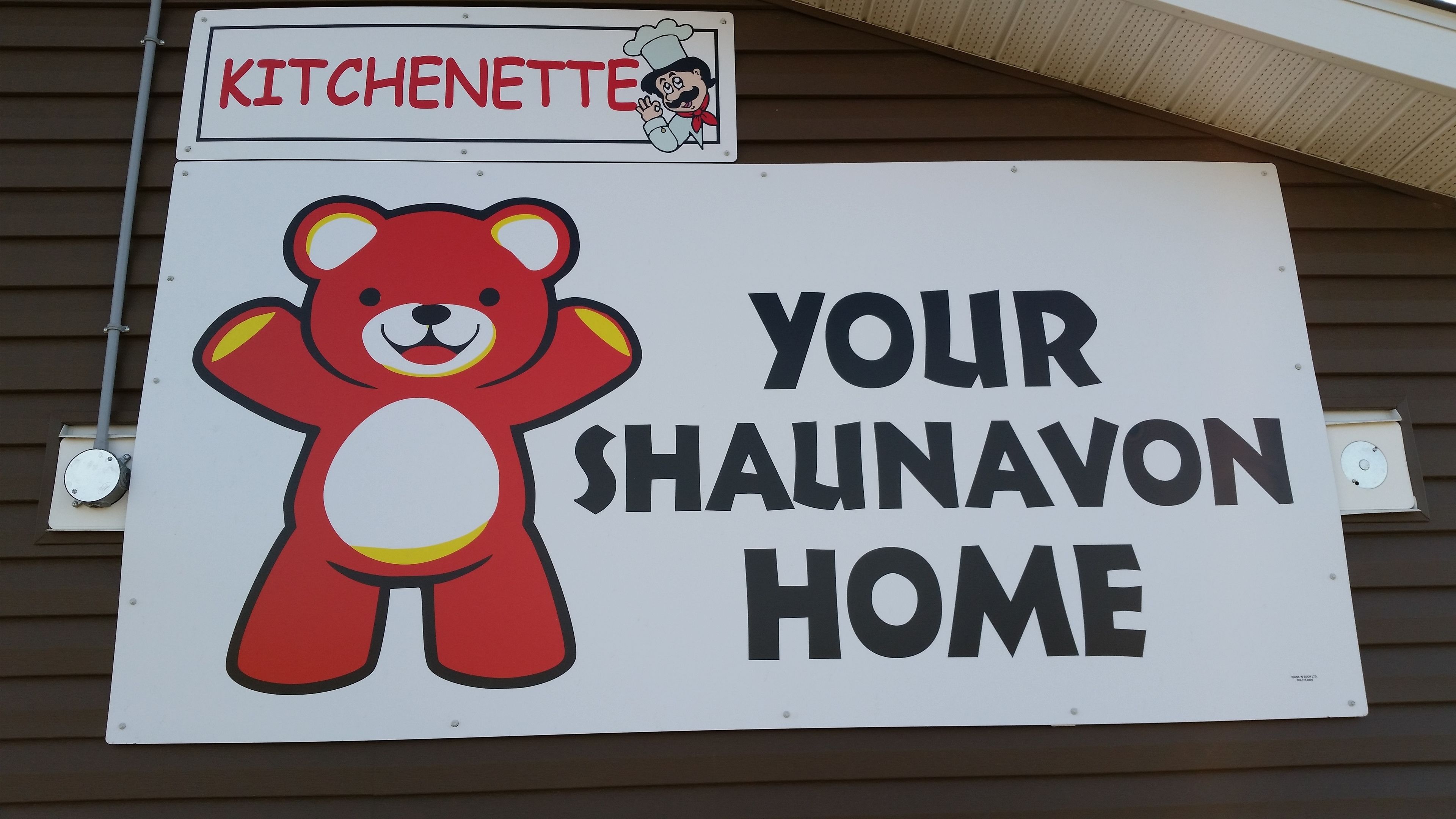 Une enseigne représentant un ours de dessin animé et portant l’inscription : « VOTRE MAISON À SHAUNAVON ».