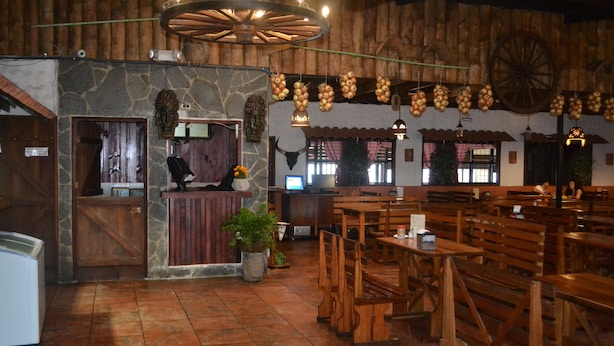 A rustic restaurant interior with stone walls, wooden benches, and hanging onions. - Hotel Las Brumas (San Rafael)