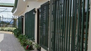 A pathway leading to a building with a tiled floor, green metal railings, and flower beds with red and pink flowers. - Hotel Las Brumas (San Rafael)