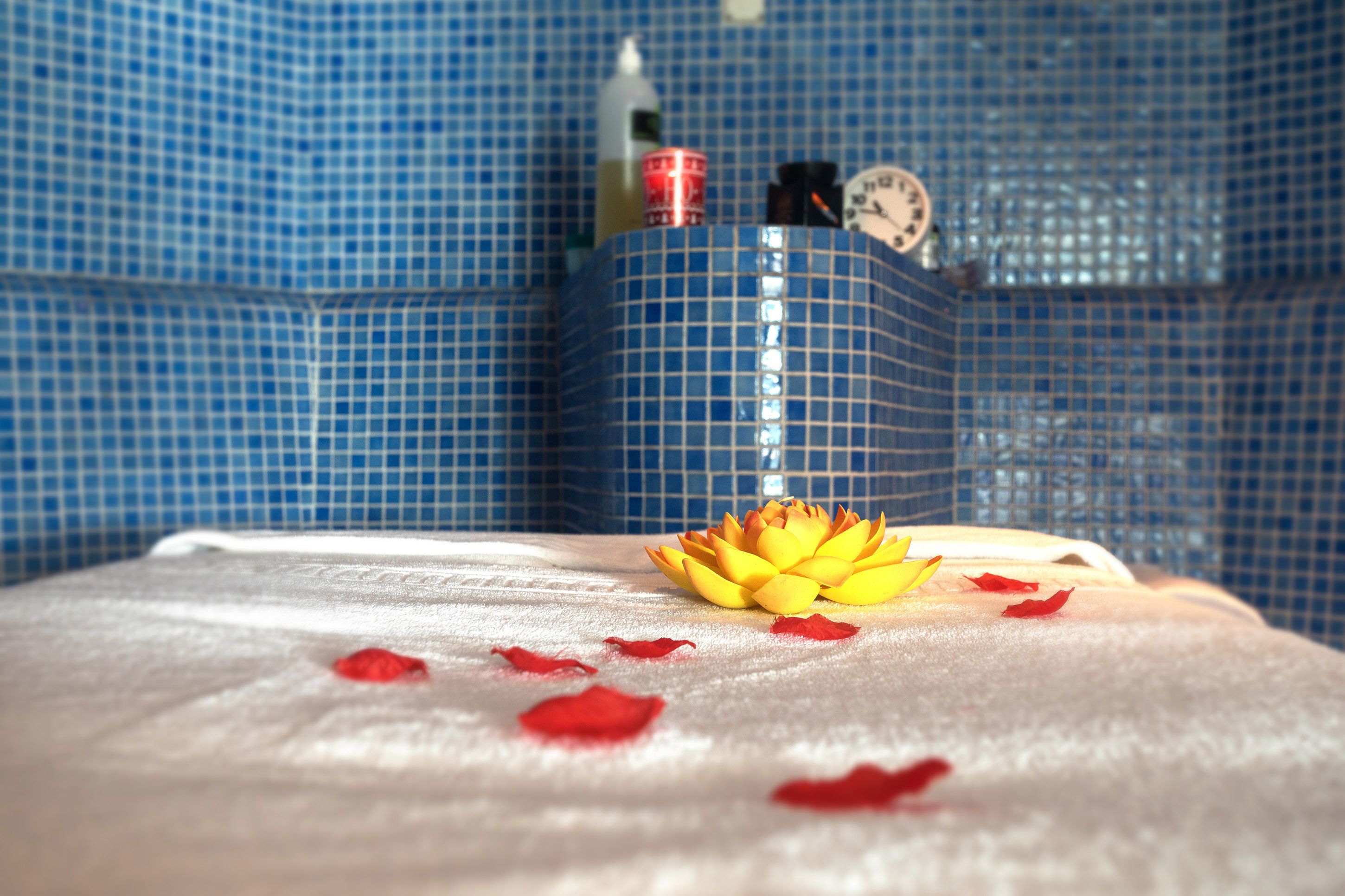 A bathroom with a blue tiled wall, a white towel, and a yellow lotus flower on the counter.