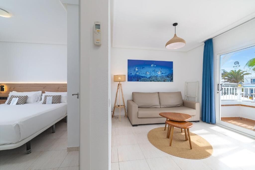 A hotel room with a bed, a sofa, a small table, a lamp, a painting, and a view of the outside.