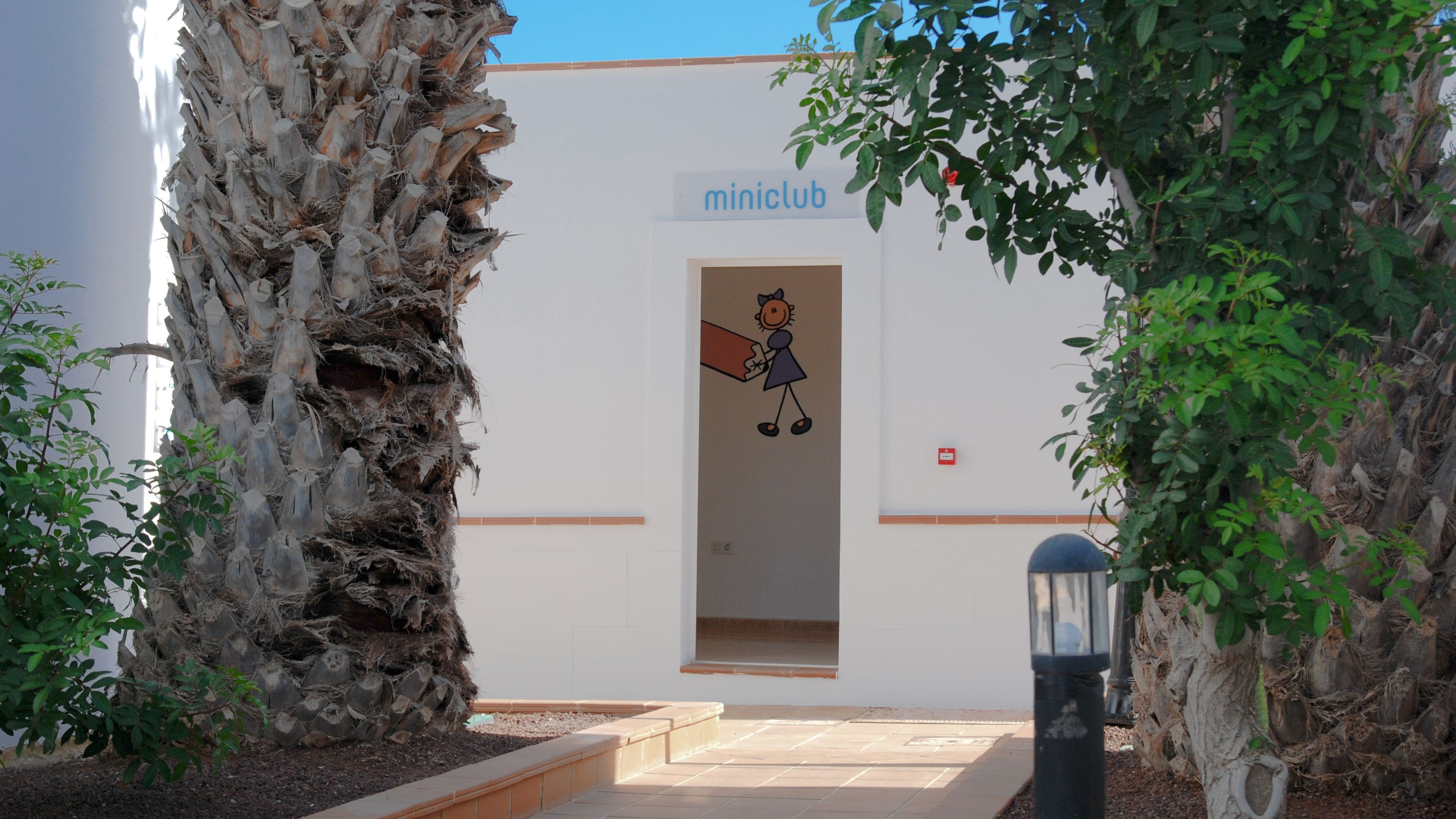 Une entrée d’immeuble avec une enseigne indiquant « miniclub », une illustration de personnage de dessin animé et une porte.