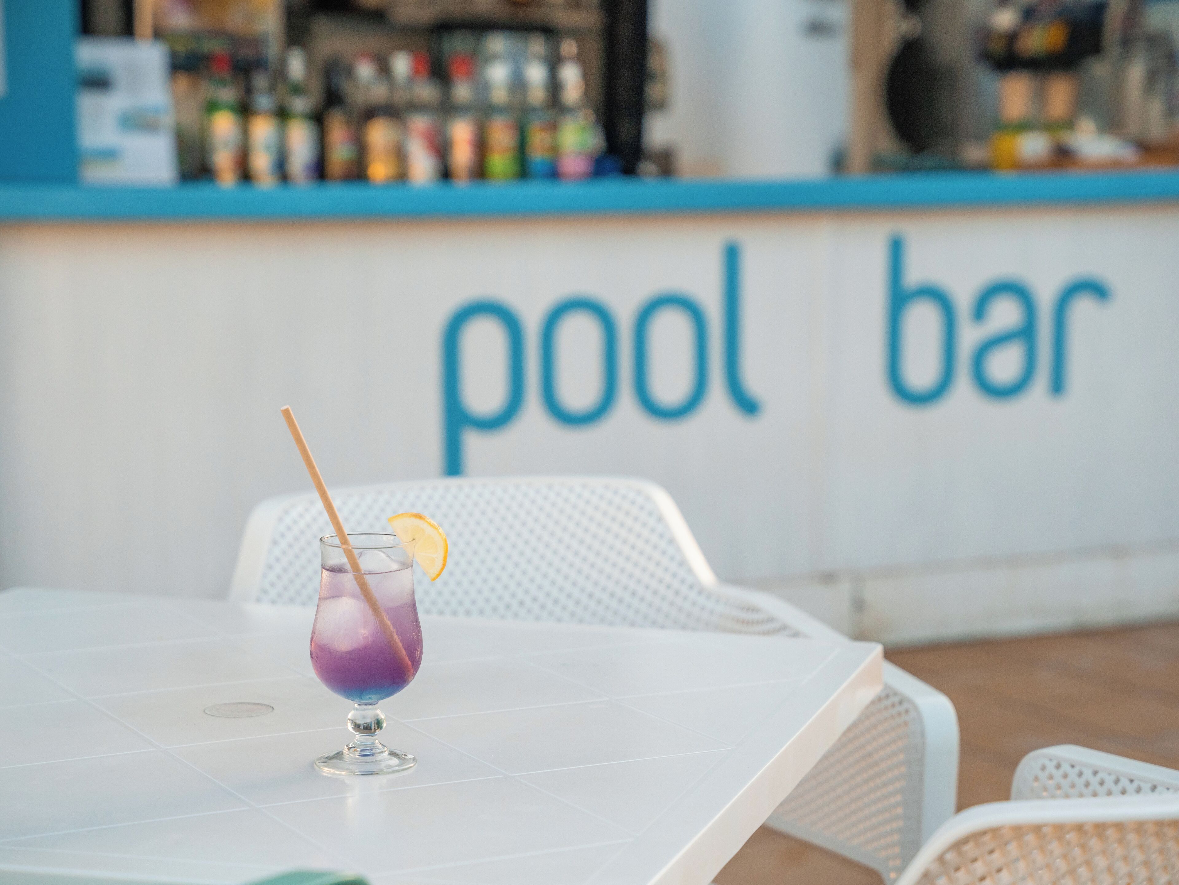 A table with a purple drink and a straw, in front of a counter with the words "pool bar" visible.