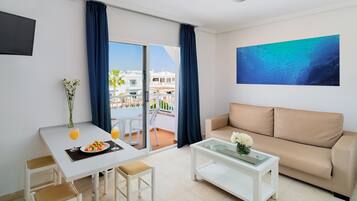 Un soggiorno moderno con un divano, un tavolo da pranzo con sedie, un tavolino e un balcone con vista su edifici e palme.