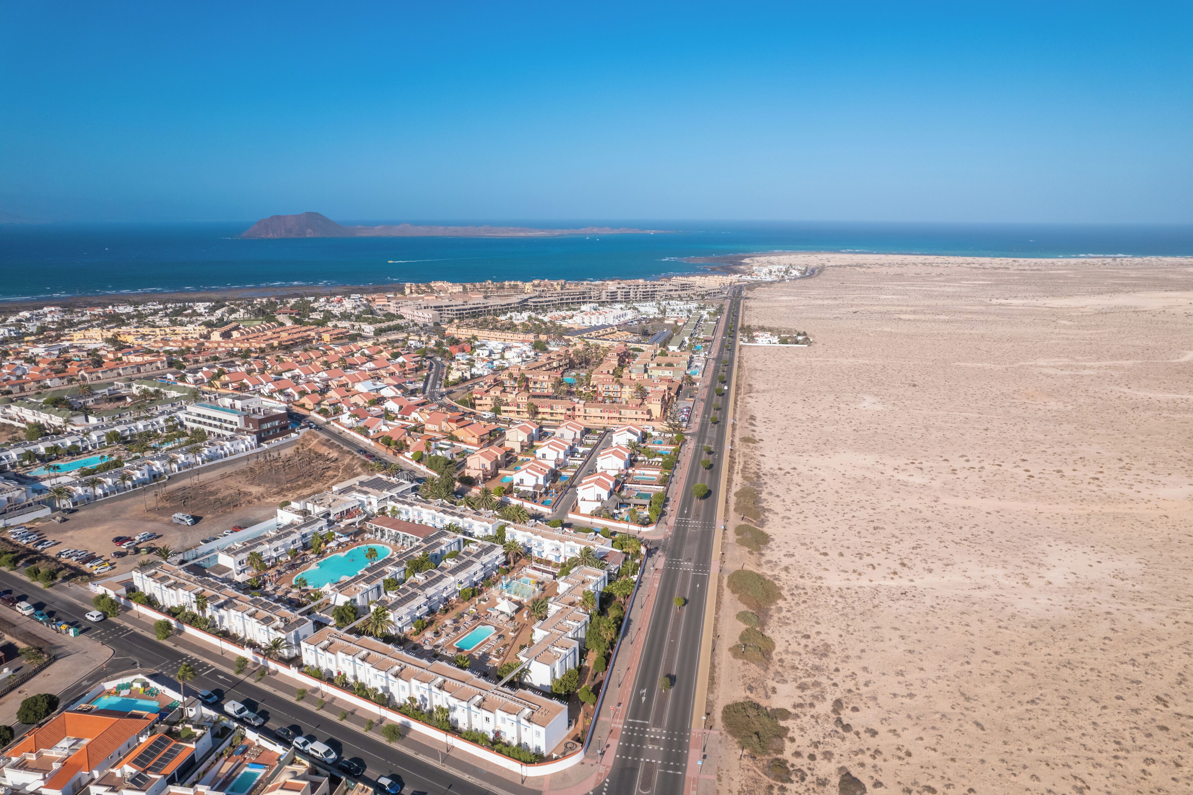 An aerial view of a coastal town with a beach, residential buildings, and a mountain in the background.