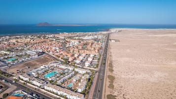 An aerial view of a coastal town with a beach, residential buildings, and a mountain in the background.