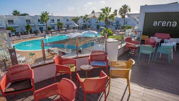 Uma área de piscina no terraço com cadeiras vermelhas e amarelas, uma piscina e vista dos edifícios ao redor.