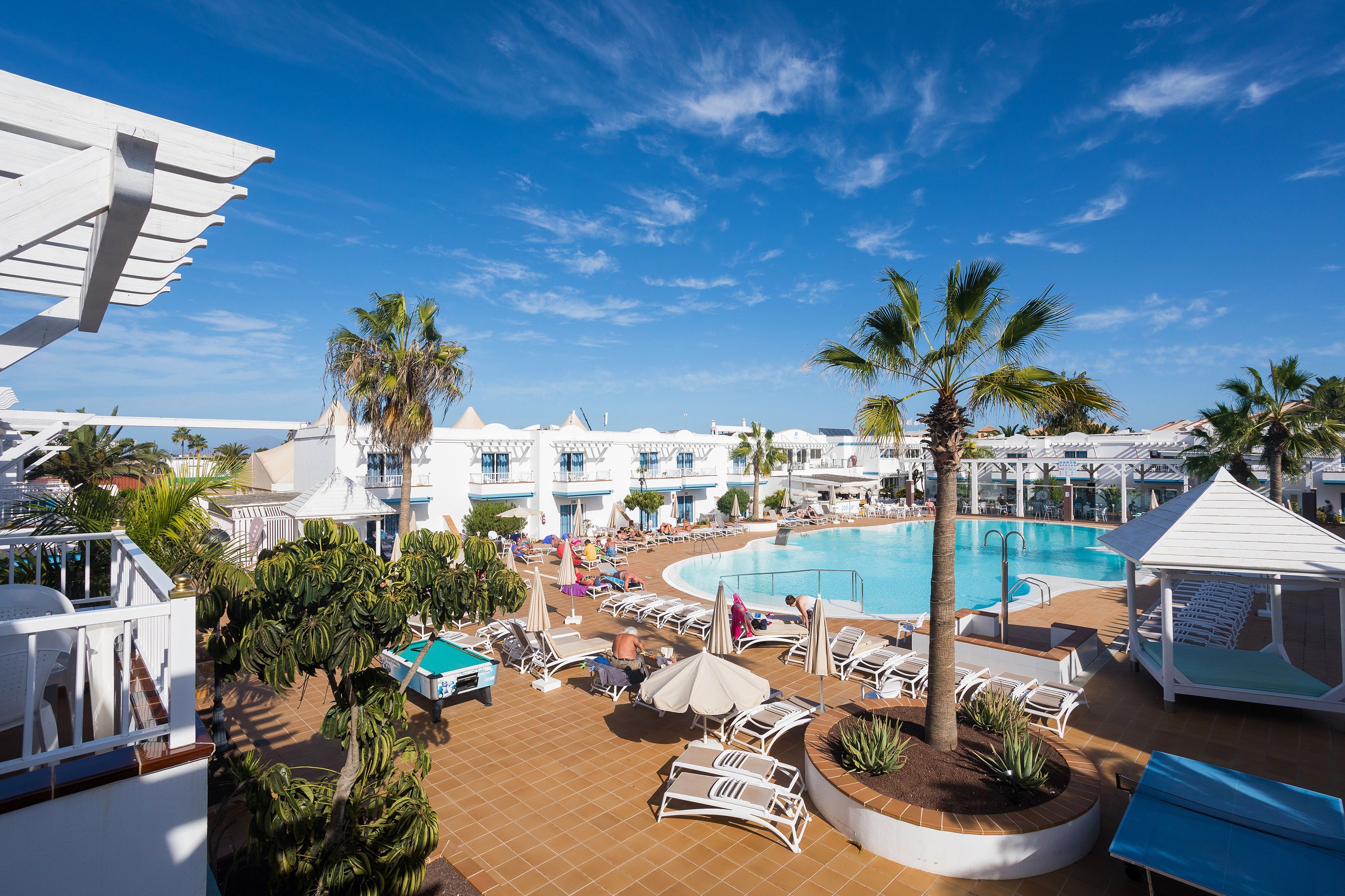 Ein Poolbereich eines Resorts mit Liegestühlen, Palmen und einem großen Schwimmbecken.