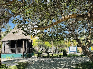 A rustic hut with a thatched roof, surrounded by lush greenery and a clear blue sky.