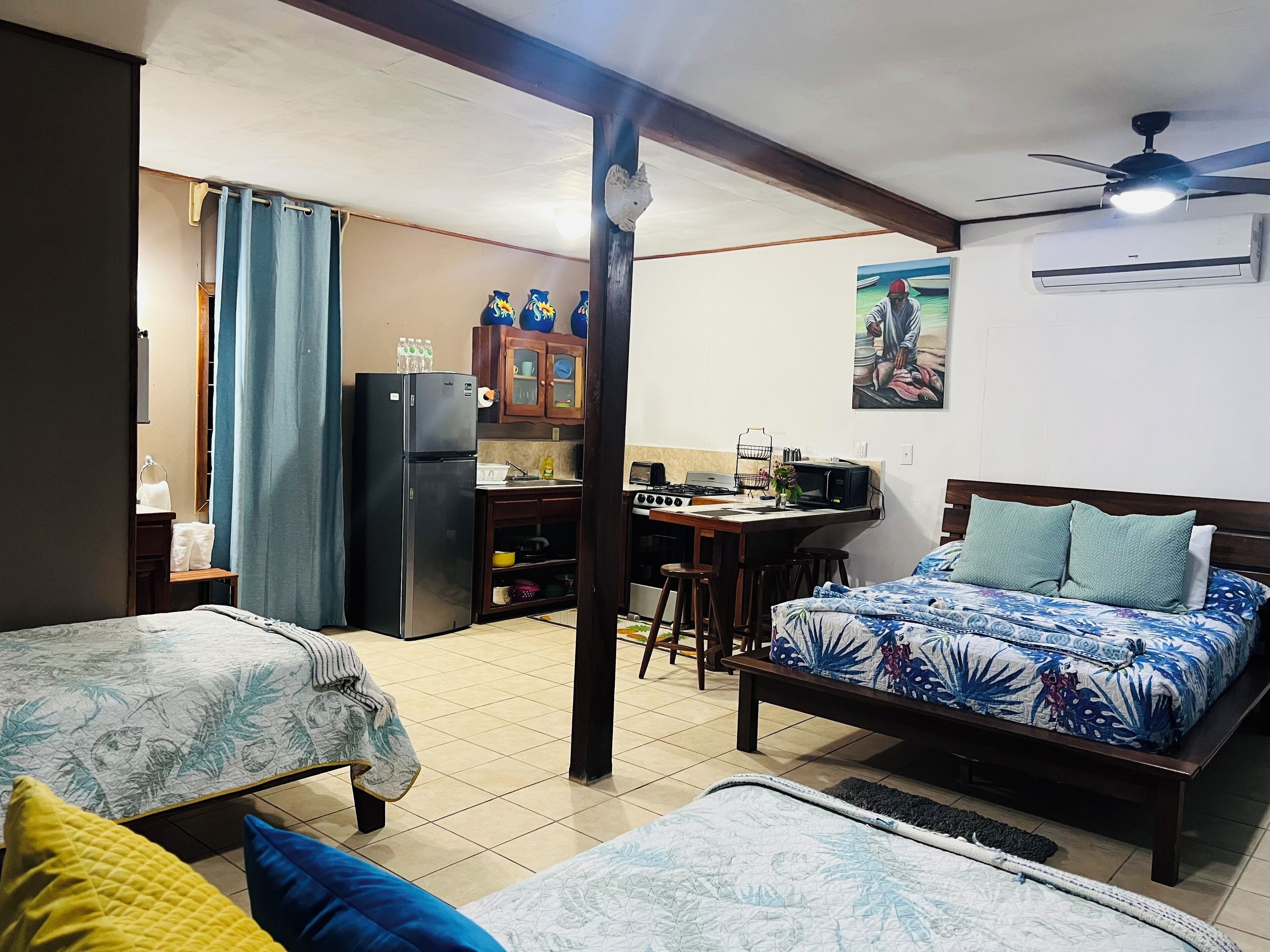 Habitación de hotel compacta con cama, kitchenette pequeño, mesa de comedor y ventilador de techo.