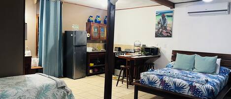Habitación de hotel compacta con cama, kitchenette pequeño, mesa de comedor y ventilador de techo.