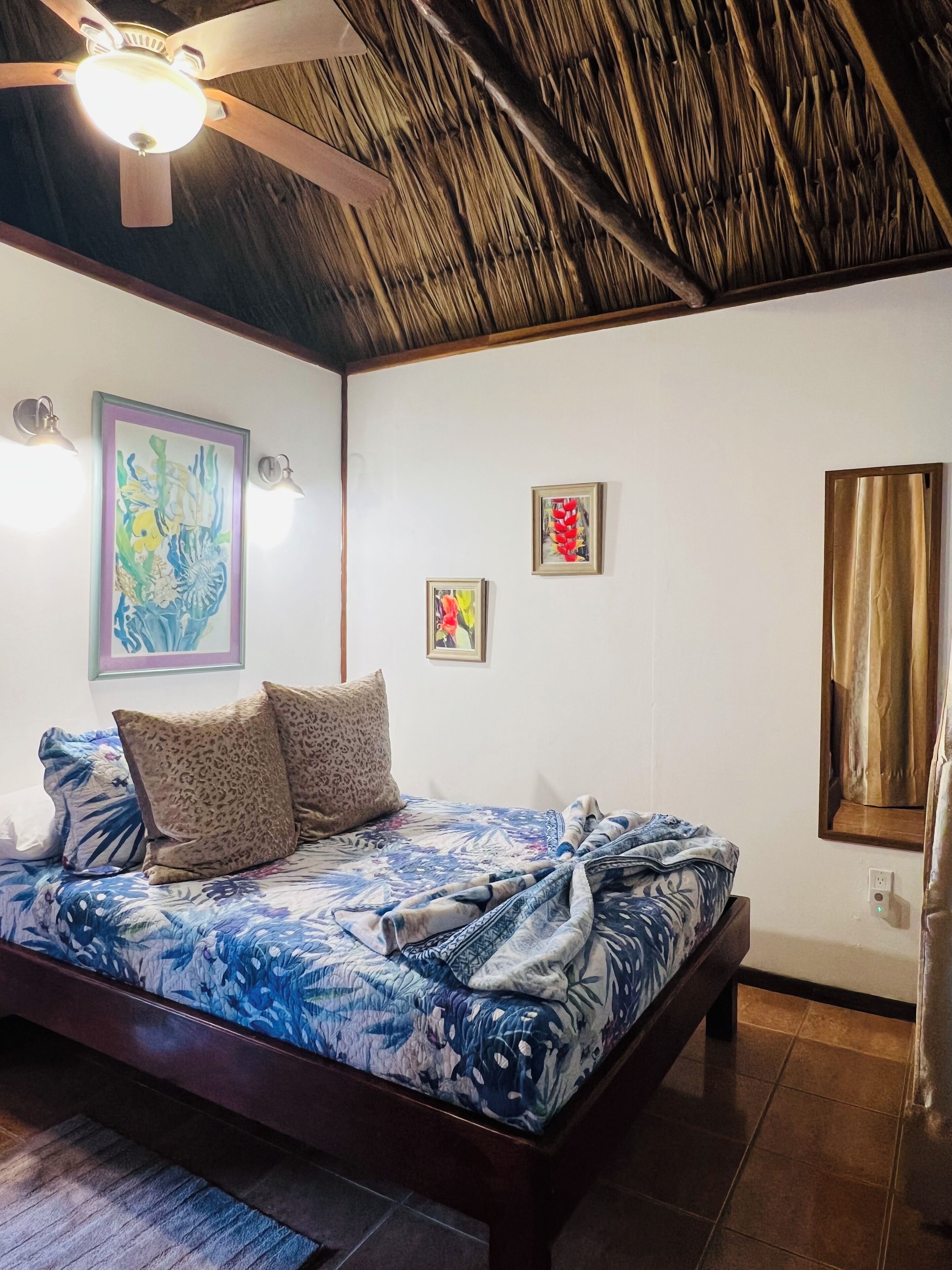 A bedroom with a bed, a ceiling fan, and artwork on the walls.