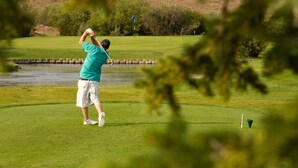 A golf course with a player in a green shirt and white shorts preparing to hit a ball. - Gannett Peak Lodge (Pinedale)