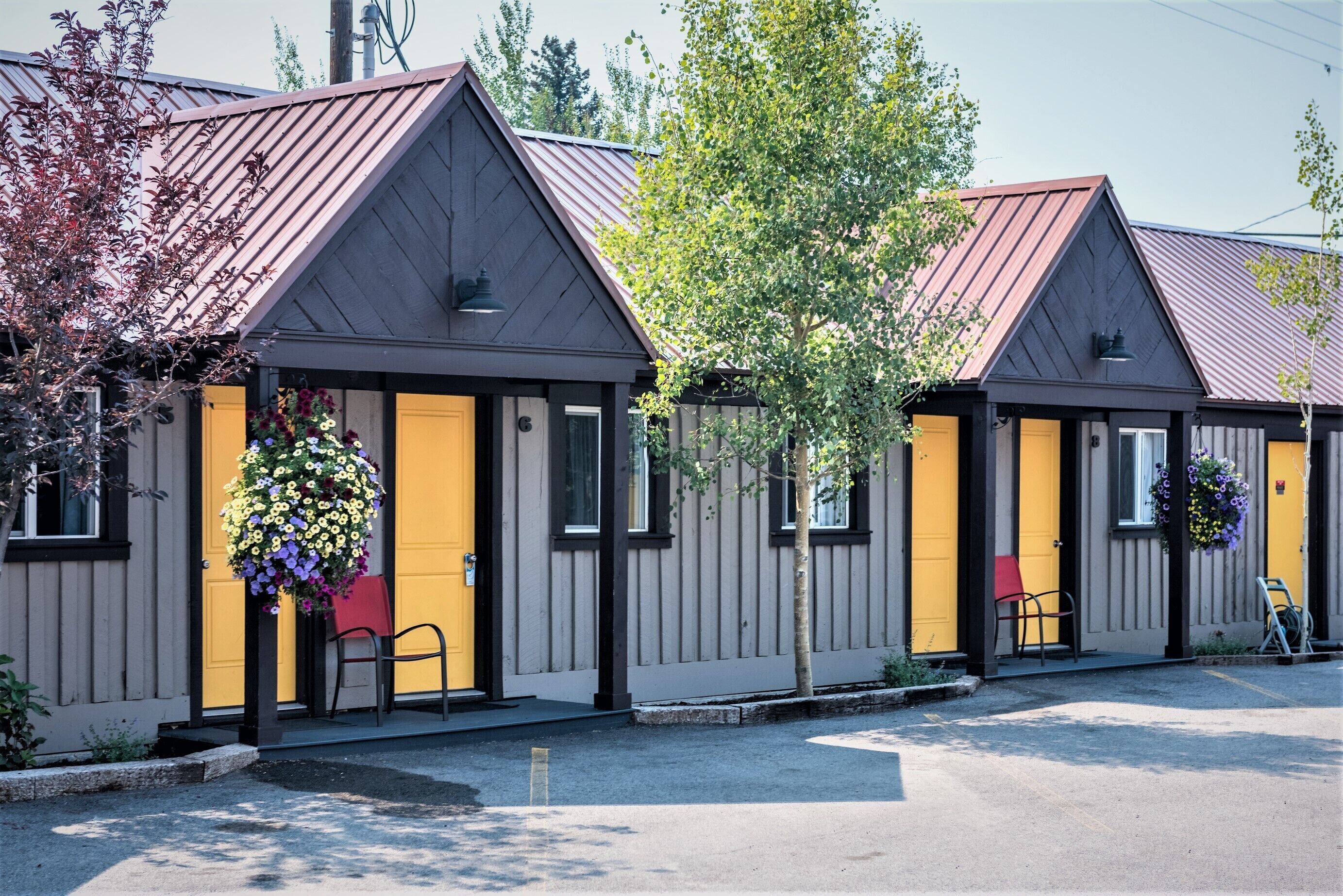 A row of two-story buildings with a dark exterior and yellow doors, each with a flower basket hanging outside.