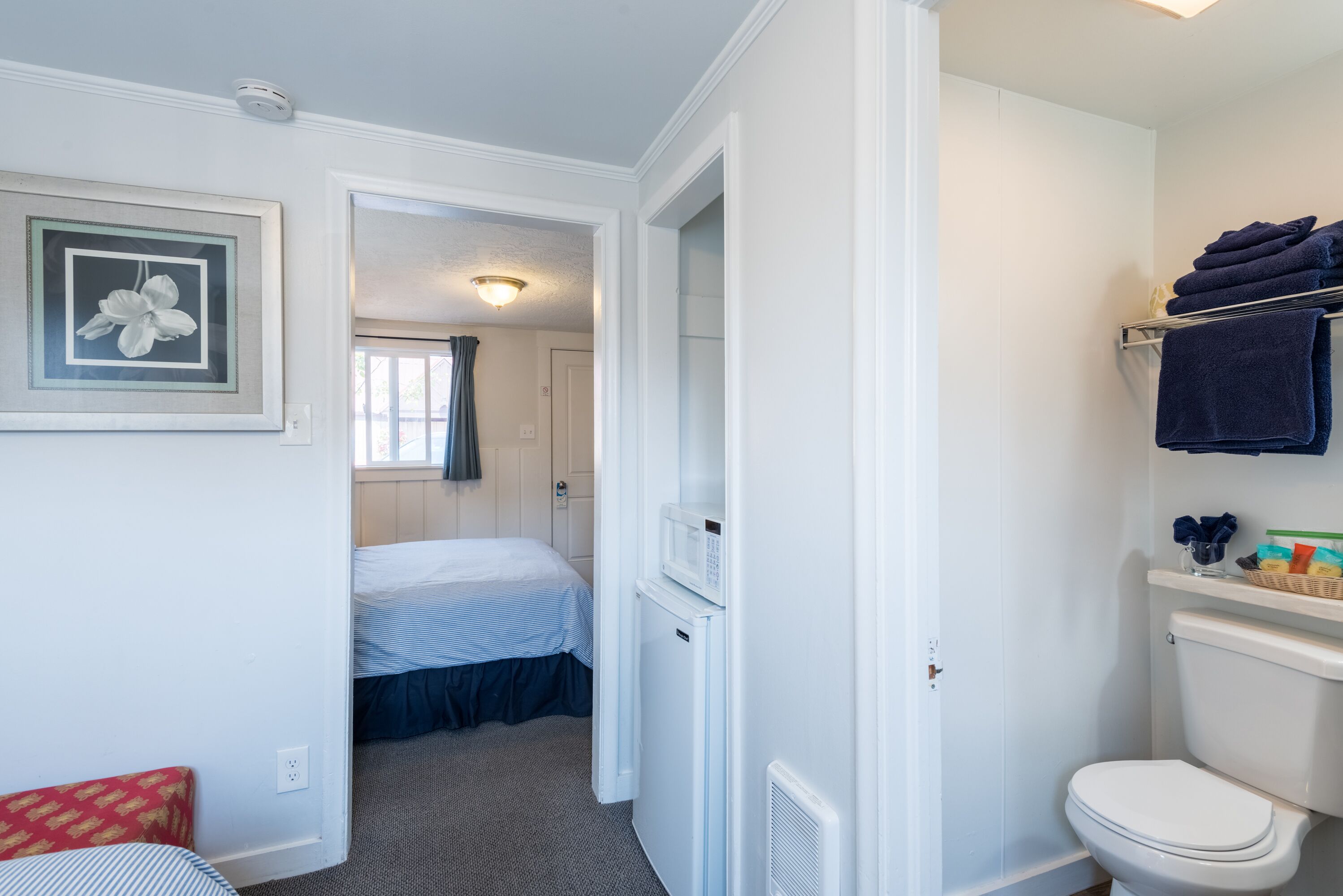 A hotel room with a bed, a small kitchenette, a toilet, and a bathroom.