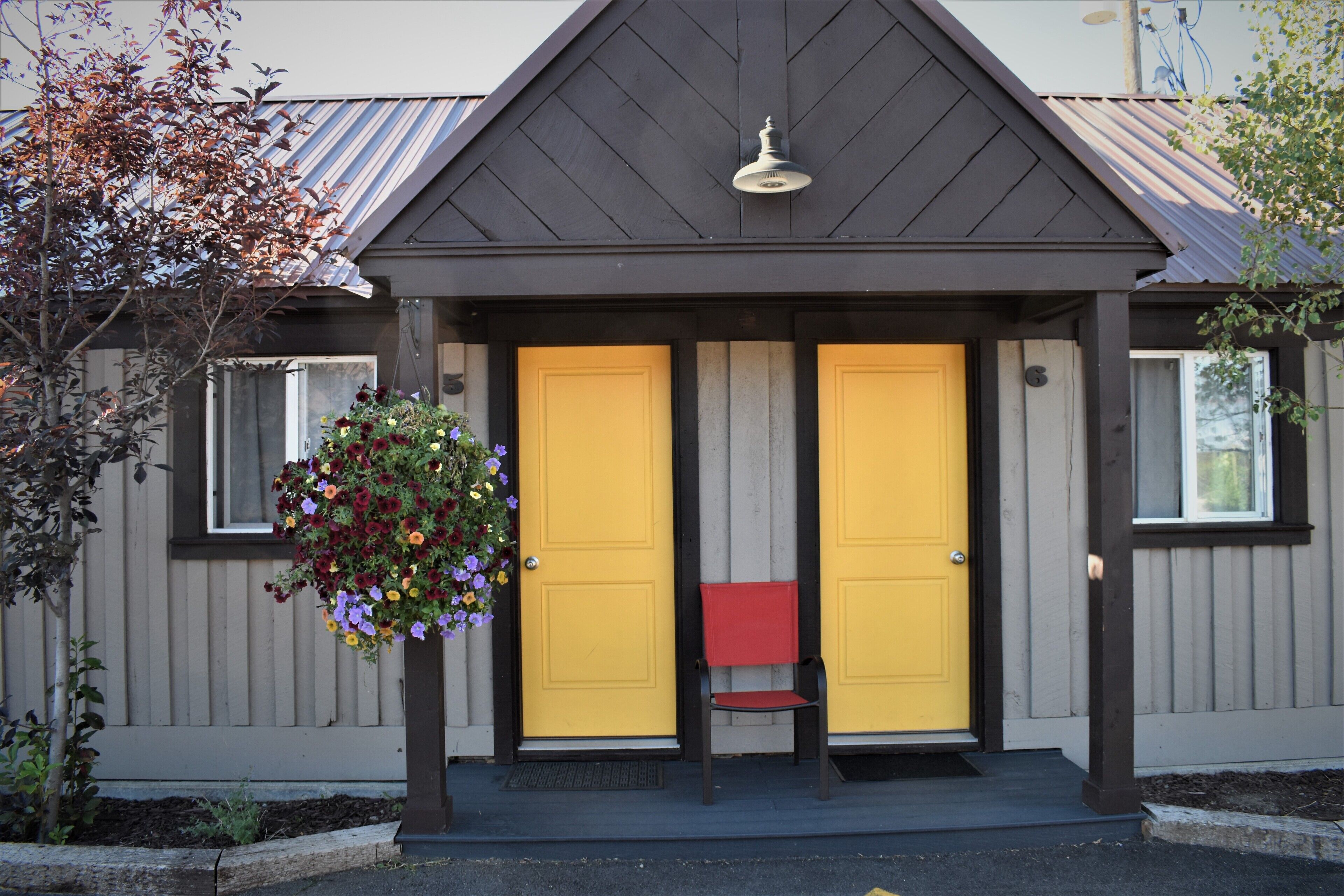 A building with two yellow doors, a red bench, and a hanging flower basket.