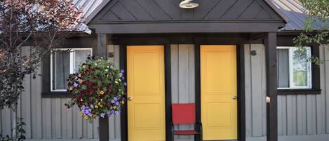 A building with two yellow doors, a red bench, and a hanging flower basket.