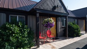 A building with a sloped roof, a hanging flower basket, and a red chair outside. - Gannett Peak Lodge (Pinedale)