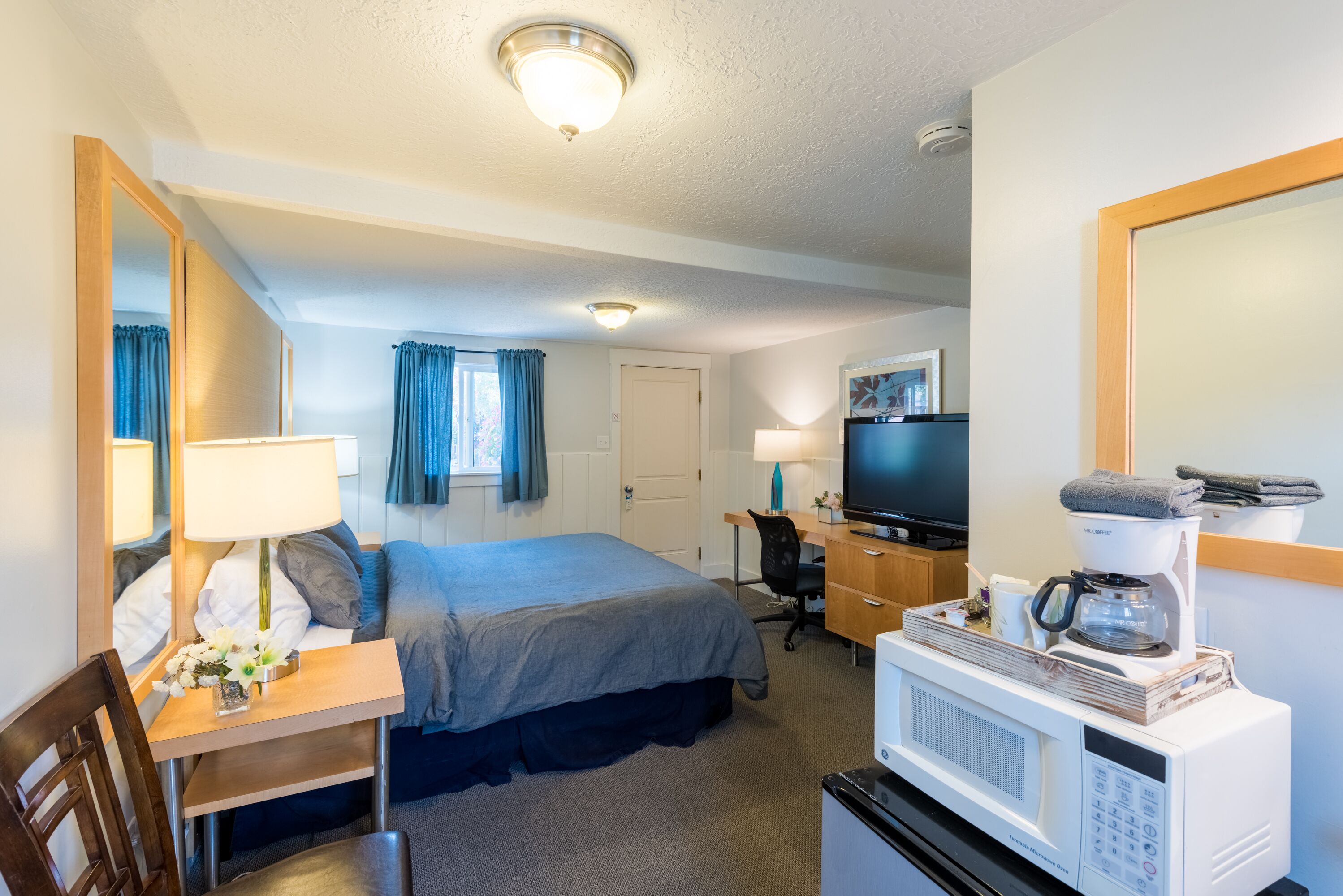 A hotel room with a bed, desk, chair, TV, microwave, and coffee maker.