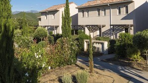 Un edificio residencial con tejado de tejas, rodeado de vegetación y con montañas al fondo.