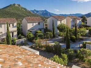 A residential area with terracotta-tiled roofs, white buildings, and a mountainous backdrop.