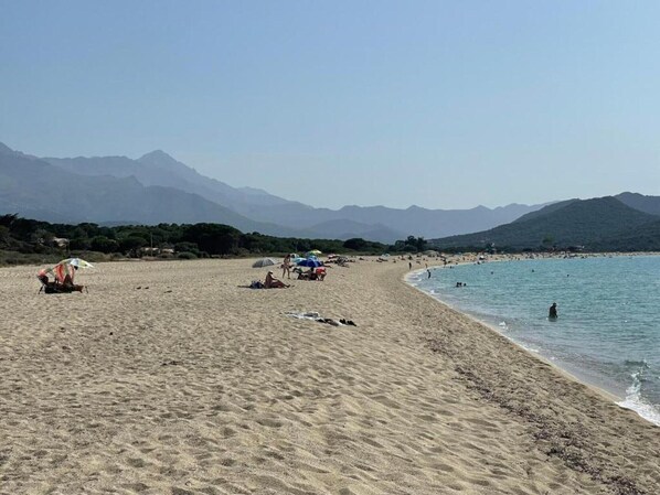 A beach with people, umbrellas, and mountains in the background.